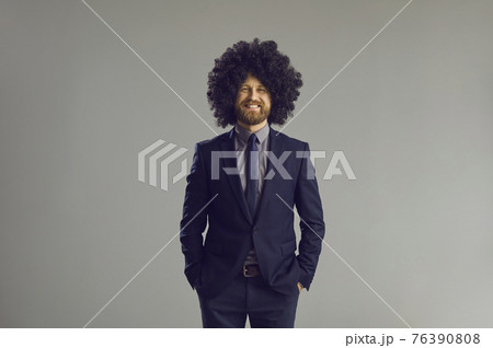 Happy guy in elegant suit and crazy curly wig standing hands in pockets and smiling 76390808