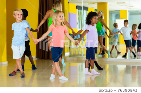 Happy kids and female teacher dancing together in studio at elementary school 76390843