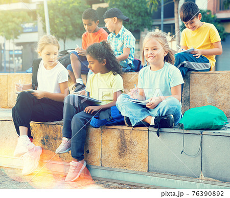 Schoolchildren sitting with workbooks in schoolyard in autumn day 76390892