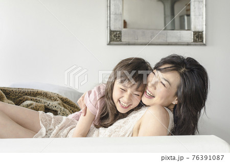 Mother and daughter laughing on sofa 76391087