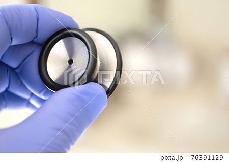 Close-up of hand in blue surgical holding stethoscope Close-up of hand in blue surgical holding stethoscope 76391129