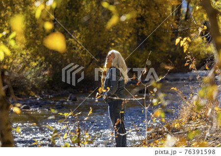 United States, Idaho, Sun Valley, Senior woman standing in sunlight by river in autumn United States, Idaho, Sun Valley, Senior woman standing in sunlight by river in autumn 76391598