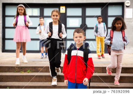 Positive boy standing near school, children on background Positive boy standing near school, children on background 76392096