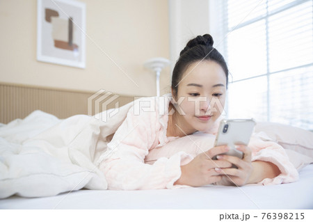 Asian woman waking up and checking smart phone 76398215
