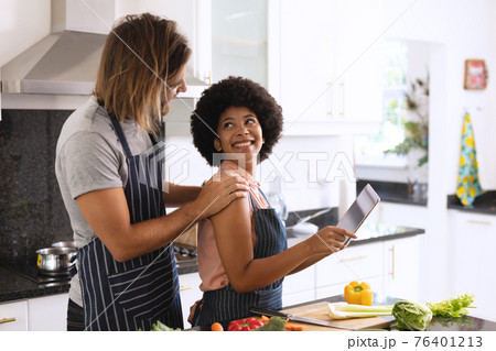 Happy diverse couple in kitchen embracing and using tablet Happy diverse couple in kitchen embracing and using tablet 76401213