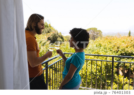 Happy diverse couple standing on balcony drinking wine Happy diverse couple standing on balcony drinking wine 76401303