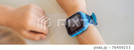 BANNER, LONG FORMAT Little boy sitting at the table and looking smart watch. Smart watch for baby safety. The child makes school lessons, listening to music, calling friends 76409253