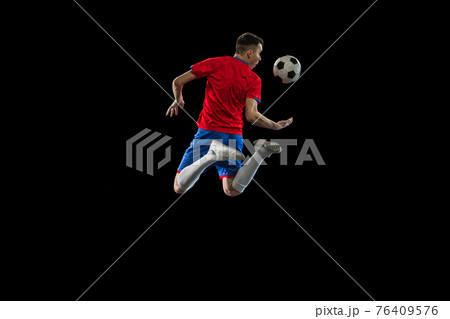 Young Caucasian soccer football player practicing isolated on black background. 76409576
