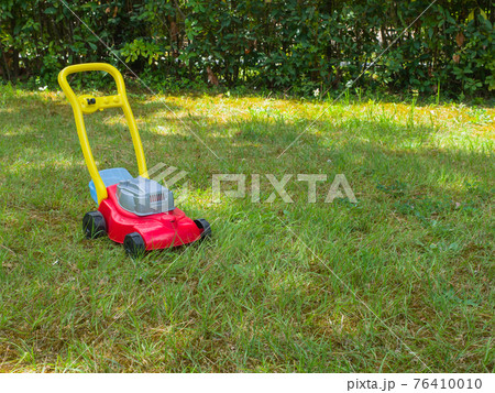 Push lawn mower toy in the middle of a garden in a sunny spring day. No people. Copy space 76410010