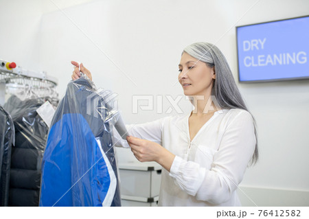 Attentive woman holding suit studying information on tag Attentive woman holding suit studying information on tag 76412582