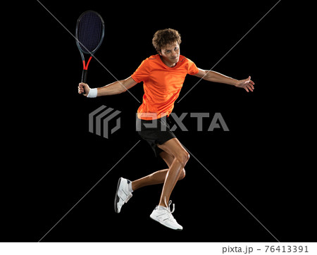 Young Caucasian man, professional tennis player training on black background. 76413391