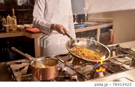 Male in plastic gloves frying peppers on fire Male in plastic gloves frying peppers on fire 76413422