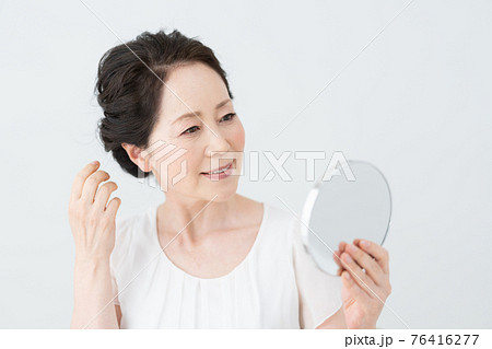 鏡を見て髪型をチェックするシニア女性の写真素材