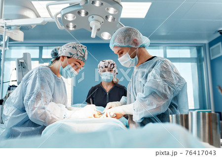 Doctors performing abdominoplasty surgery in the hospital. Focus on male plastic surgeon doing abdominal plastic surgery in operating room. Concept of tummy tuck and cosmetic surgery. 76417043