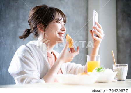 朝食を食べながらスマホを使う若い女性 朝食を食べながらスマホを使う若い女性 76429677