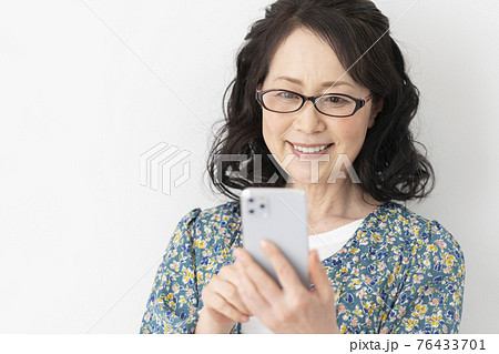 スマートフォンを操作するメガネをかけた笑顔の60代の女性 スマートフォンを操作するメガネをかけた笑顔の60代の女性 76433701
