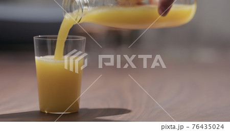 man pour organic orange juice from glass bottle into tumbler glass on walnut table man pour organic orange juice from glass bottle into tumbler glass on walnut table 76435024