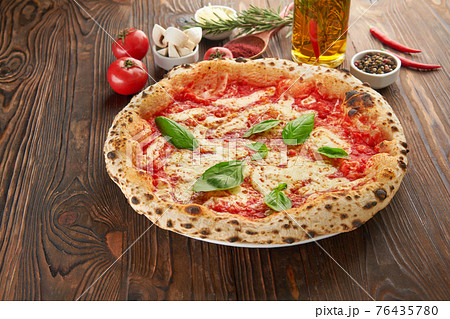 Original italian neapolitan pizza Margherita with melted mozzarella cheese, fresh basil leaves and tomato sauce on wooden table with ingredients. Fast food italian menu and vegetarian eating concept Original italian neapolitan pizza Margherita with melted mozzarella cheese, fresh basil leaves and tomato sauce on wooden table with ingredients. Fast food italian menu and vegetarian eating concept 76435780