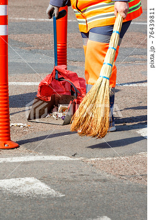 Woman janitor collects garbage from the sidewalk on a sunny day. 76439811