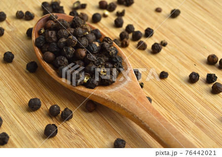 Aromatic fresh peppercorns in spoon on wooden bamboo cutting board 76442021