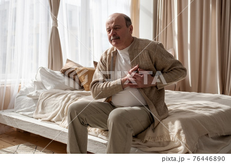 Old man with heart attack sitting alone at home. 76446890