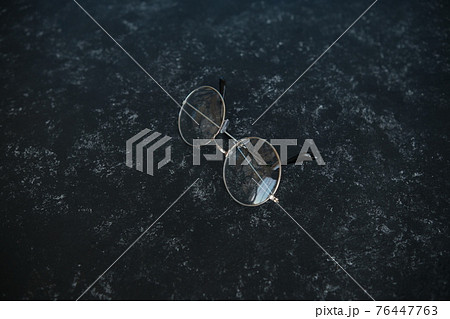 Silver metal glasses. On a solid black stone background. With a soft blurred electoral background. Eyepieces, Vision. top view Silver metal glasses. On a solid black stone background. With a soft blurred electoral background. Eyepieces, Vision. top view 76447763