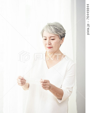 Senior asian woman wearing facemask during coronavirus and flu outbreak. Virus and illness protection, home quarantine. COVID-19. Taking on or taking off masks. Senior asian woman wearing facemask during coronavirus and flu outbreak. Virus and illness protection, home quarantine. COVID-19. Taking on or taking off masks. 76449844