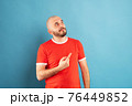 A middle-aged man with a beard in a red T-shirt on a blue background stands rejoicing in victory. Isolated. 76449852