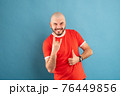 A middle-aged man with a beard in a blue T-shirt on a red background stands rejoicing in victory. Isolated. 76449856