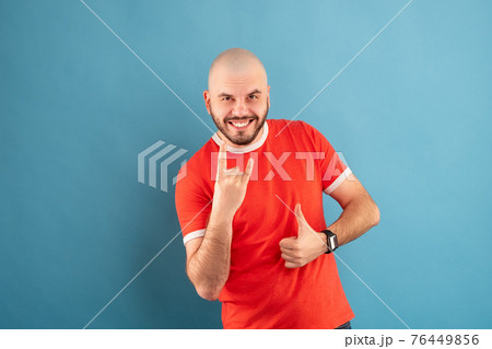 A middle-aged man with a beard in a blue T-shirt on a red background stands rejoicing in victory. Isolated. A middle-aged man with a beard in a blue T-shirt on a red background stands rejoicing in victory. Isolated. 76449856
