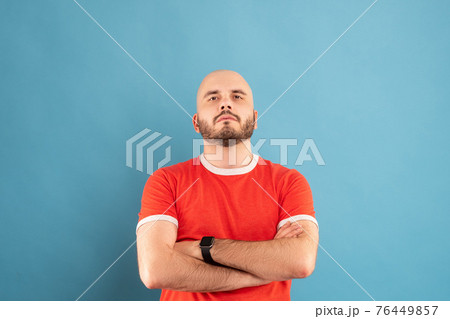 A middle-aged man with a beard in a red T-shirt on a blue background stands with his arms outstretched and rejoices in victory. Isolated. A middle-aged man with a beard in a red T-shirt on a blue background stands with his arms outstretched and rejoices in victory. Isolated. 76449857