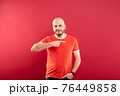 A middle-aged man with a beard in a red T-shirt on a red background stands rejoicing in victory. Isolated. 76449858