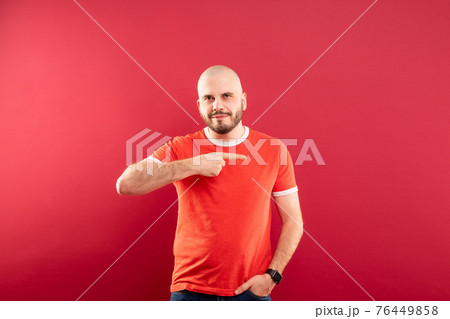 A middle-aged man with a beard in a red T-shirt on a red background stands rejoicing in victory. Isolated. 76449858