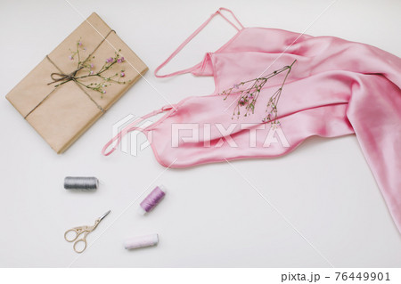 Composition with pink silk fabric, gift in craft paper and threads and scissors on white background. Flat lay, top view. Hobby, leisure concept. Composition with pink silk fabric, gift in craft paper and threads and scissors on white background. Flat lay, top view. Hobby, leisure concept. 76449901