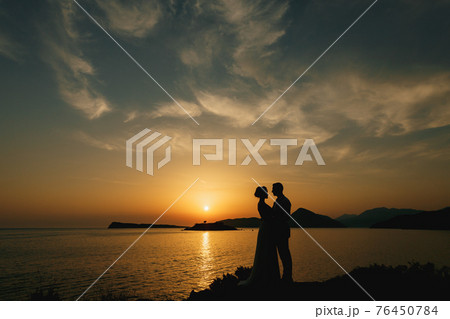 The bride and groom are embracing on the seashore at sunset and look at each other The bride and groom are embracing on the seashore at sunset and look at each other 76450784