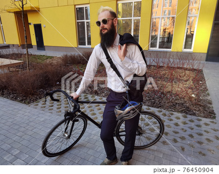 A young stylish businessman pushing a bicycle while going to work. 76450904