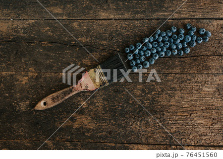 A paintbrush in blue paint lies near blueberries 76451560
