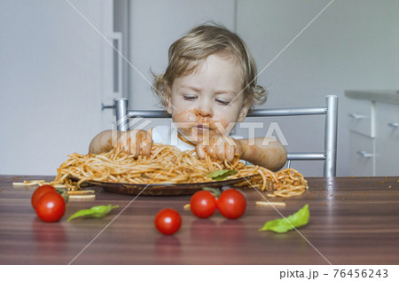 Funny baby child getting messy eating spaghetti with tomato sauce from a large plate, by itself with his hands, at home Funny baby child getting messy eating spaghetti with tomato sauce from a large plate, by itself with his hands, at home 76456243
