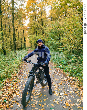 A sporty man on an electric fat bike in the woods. Super hobby. Ecological transport. 76467656