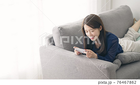 ソファに寝転がってスマホを見る女性 ソファに寝転がってスマホを見る女性 76467862