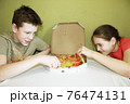children a boy and a girl eat pizza sitting at the table 76474131