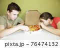 children a boy and a girl eat pizza sitting at the table 76474132