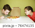 children a boy and a girl eat pizza sitting at the table 76474135