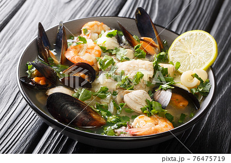 Paila marina is a traditional Chilean stew consisting of a shellfish stock combined with a variety of seafood, shellfish, herbs, spices, and vegetables close-up in a bowl. horizontal 76475719