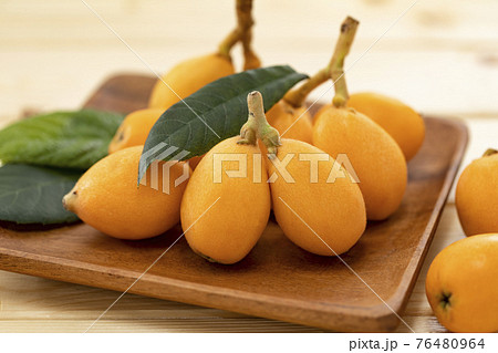 木目のテーブルに葉を添えて並べたビワ_背景ぼかし 76480964