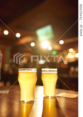 Two glasses full of fresh foamy beer on counter Two glasses full of fresh foamy beer on counter 76482006