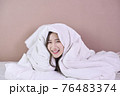 Cheerful young woman lying on bed playing with blanket and looking at camera. Asian girl feeling fresh after nap on bed. Laughing woman having fun while embracing pillow and blanket. 76483374