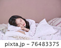 Beautiful young Asian woman lying down in the bed and sleeping. Teen girl with closed eyes covers her face with white blanket in the morning 76483375