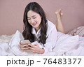 Young smiling Asian woman using smartphone for play game or buying online shopping 76483377