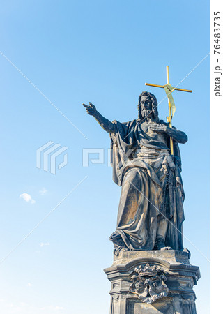 Ancient statue of a saint monk with a cross at the Charles Bridge in Prague at blue sky and copy space, Czech Republic, summer, closeup Ancient statue of a saint monk with a cross at the Charles Bridge in Prague at blue sky and copy space, Czech Republic, summer, closeup 76483735